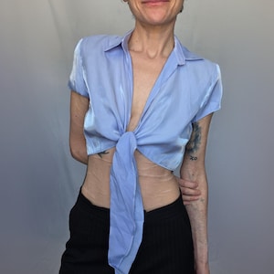 A woman wearing a blue shirt with a tie, posing with a smile and looking to her left.