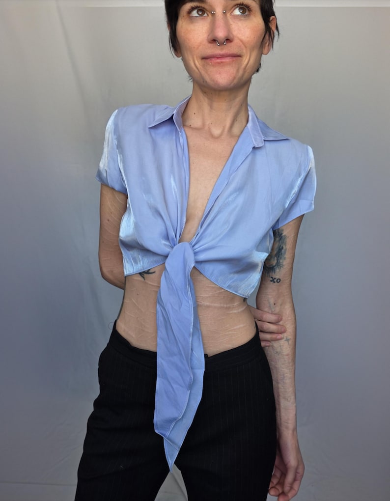 A woman wearing a blue shirt with a tie, posing with a smile and looking to her left.