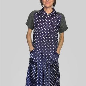 Peut inclure: Une robe arrivant aux genoux en tissu bleu foncé à pois blancs, dotée d'un col, de manches courtes grises et de deux poches avant. Le vêtement présente une fermeture boutonnée sur le devant et une coupe droite et décontractée sur tout le corps.