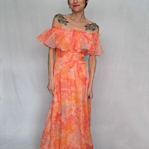 A woman wearing a long, off-the-shoulder dress with a floral print stands against a white background.
