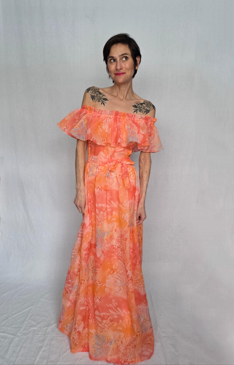 A woman wearing a long, off-the-shoulder dress with a floral print stands against a white background.