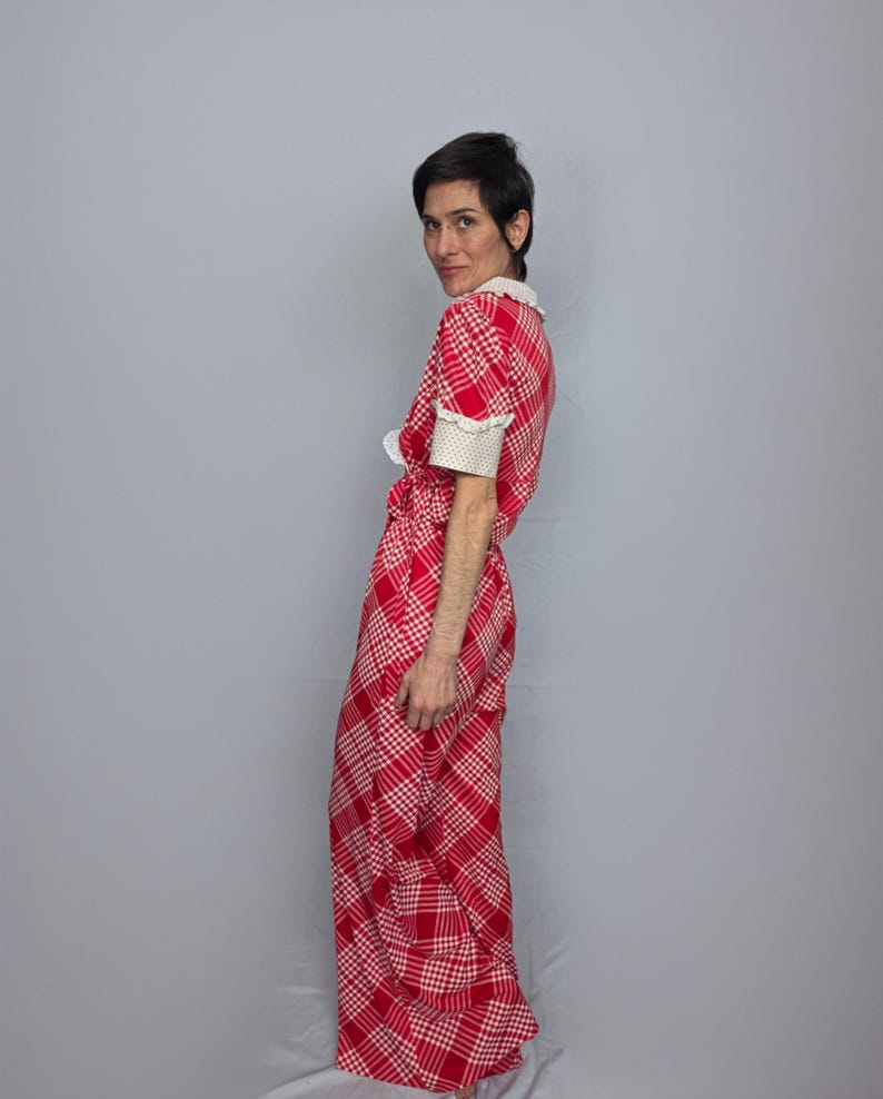 A woman wearing a red and white checkered dress stands against a gray background, looking over her shoulder.