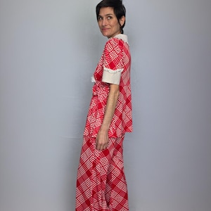 A woman wearing a red and white checkered dress stands against a gray background, smiling at the camera.