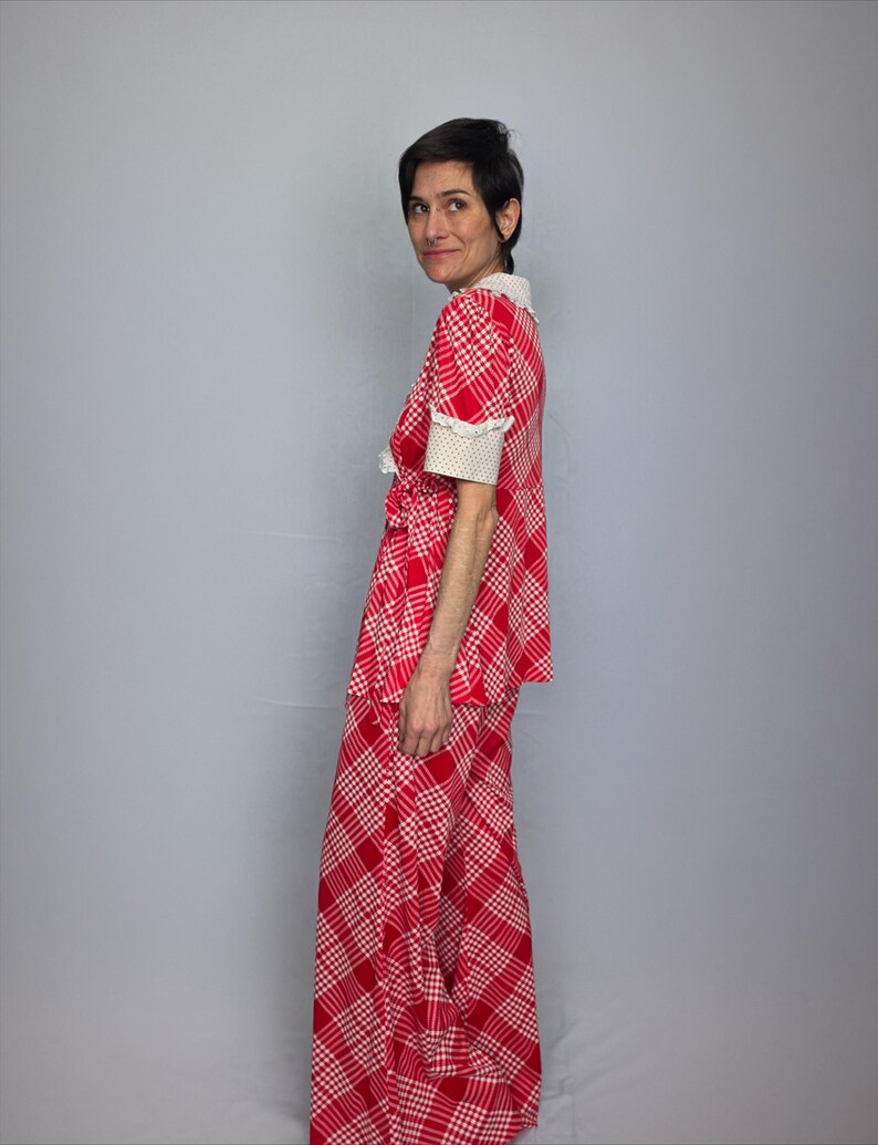 A woman wearing a red and white checkered dress stands against a gray background, smiling at the camera.