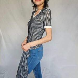 May include: A black and white patterned mesh top with a white trim around the neckline and short sleeves. The top is paired with blue jeans.