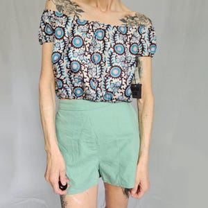 May include: An off-the-shoulder crop top with a floral pattern in blue, brown, and white, paired with mint green shorts. The top has short sleeves and a fitted silhouette. The shorts are high-waisted.