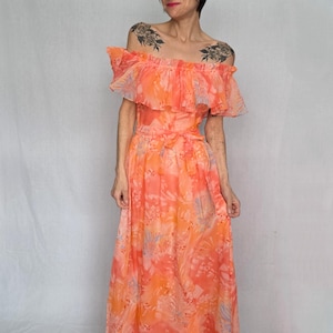 A woman wearing a long, off-the-shoulder dress with a floral print stands against a white background.