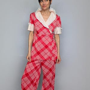 A woman wearing a red and white checkered dress with a lace collar and sleeves stands against a gray background.