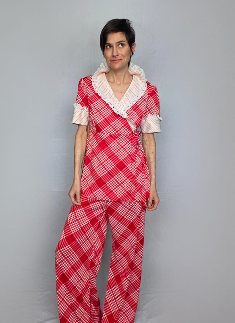 A woman wearing a red and white checkered dress with a lace collar and sleeves stands against a gray background.