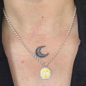 Op de afbeelding: Zilveren ketting met een kleine schedel hanger. De schedel hanger heeft een goudkleurig gezicht en een zilveren omtrek. De ketting wordt om de nek gedragen.