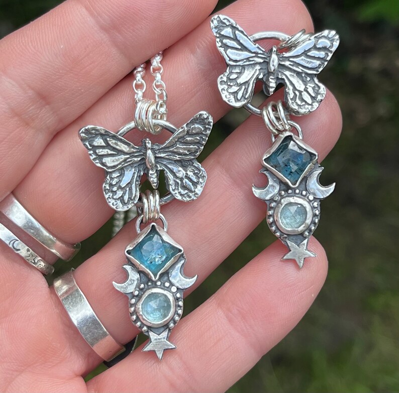 May include: Two silver necklaces with butterfly charms and blue gemstone pendants. Each pendant features a crescent moon design and a star.