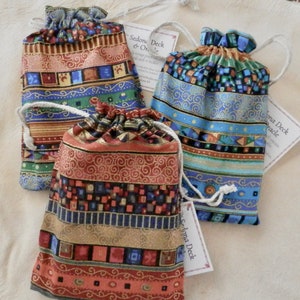 May include: Three colourful drawstring bags with gold trim and geometric patterns. Each bag has a tag that reads "Sedona Deck & Oracle".