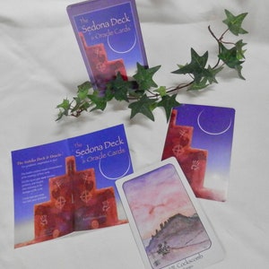 May include: A set of oracle cards with a purple and blue background. The cards feature a red rock formation with symbols and the text "The Sedona Deck & Oracle Cards".