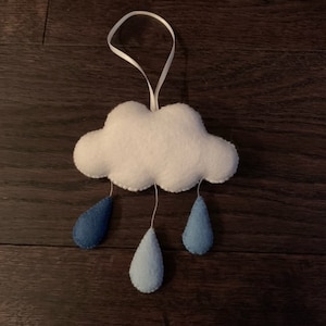 Peut inclure: Un nuage en feutre blanc avec trois gouttes de pluie en feutre bleu qui pendent. Le nuage a une boucle blanche pour l'accrocher.