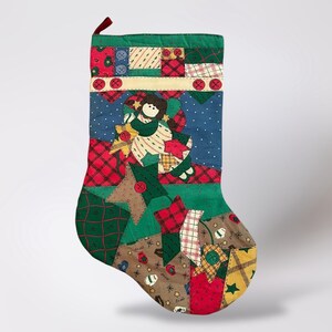 Puede incluir: Un calcetín navideño acolchado con un diseño de patchwork en rojo, verde, azul y marrón. El calcetín presenta una aplicación de ángel y adornos de botones. La parte superior tiene un borde verde y un lazo rojo para colgar.