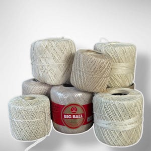 May include: A collection of off-white crochet yarn balls, some wrapped in clear plastic. One ball has a red and white label that reads "BIG BALL". The yarn is tightly wound, and the balls are stacked together.