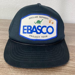 May include: Black and blue trucker hat with a white patch that says "Sinclair Refinery Ebasco Project Team" and features a green dinosaur.