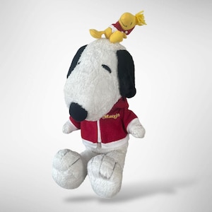May include: A plush Snoopy dog wearing a red hoodie with the Macy's logo, and a yellow Woodstock bird on top. The Snoopy plush has black ears and nose, and white fur. The Woodstock bird is yellow with red accents.