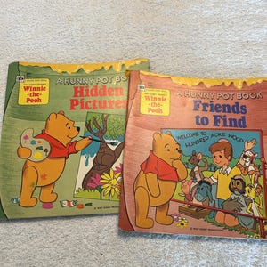 May include: Two Winnie the Pooh Golden Shape books titled A Hunny Pot Book: Hidden Pictures and A Hunny Pot Book: Friends to Find. The covers feature illustrations of Winnie the Pooh, Christopher Robin, and other characters with honey-drip borders.