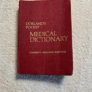 May include: A red hardcover book titled "Dorland's Pocket Medical Dictionary, Twenty-Second Edition." The text is in gold lettering. The book is closed and lying flat.