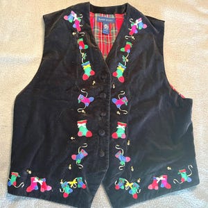 May include: A black velvet vest featuring embroidered colorful Christmas stockings and small gold beads. The vest has a button-front closure and a red, green, and blue plaid lining. A label inside the collar reads Karen Scott.