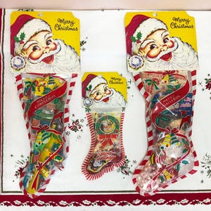 May include: Three Christmas stockings filled with candy, each with a Santa Claus head on a yellow tag that reads "Merry Christmas." The stockings are red and white striped, with a red ribbon and the words "Merry Christmas" on the front.