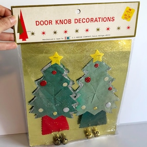 May include: A package of vintage Christmas door knob decorations. The package features two green felt Christmas trees with red and white accents, yellow star toppers, and gold bells. The package reads "DOOR KNOB DECORATIONS".