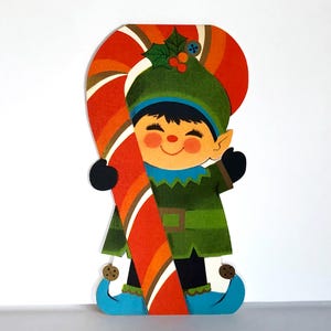 May include: A vintage Christmas card featuring a smiling elf holding a large candy cane. The elf wears a green outfit, blue hat, and shoes. The candy cane has red, orange, and white stripes. The card has a retro, cartoonish style.