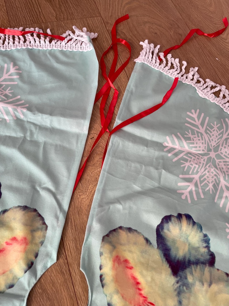 Pode incluir: Duas saias de &aacute;rvore de Natal de tecido azul claro com desenhos de flocos de neve brancos e uma borda de croch&ecirc; branca. Fitas vermelhas s&atilde;o anexadas para amarrar. A parte inferior das saias apresenta um design colorido.