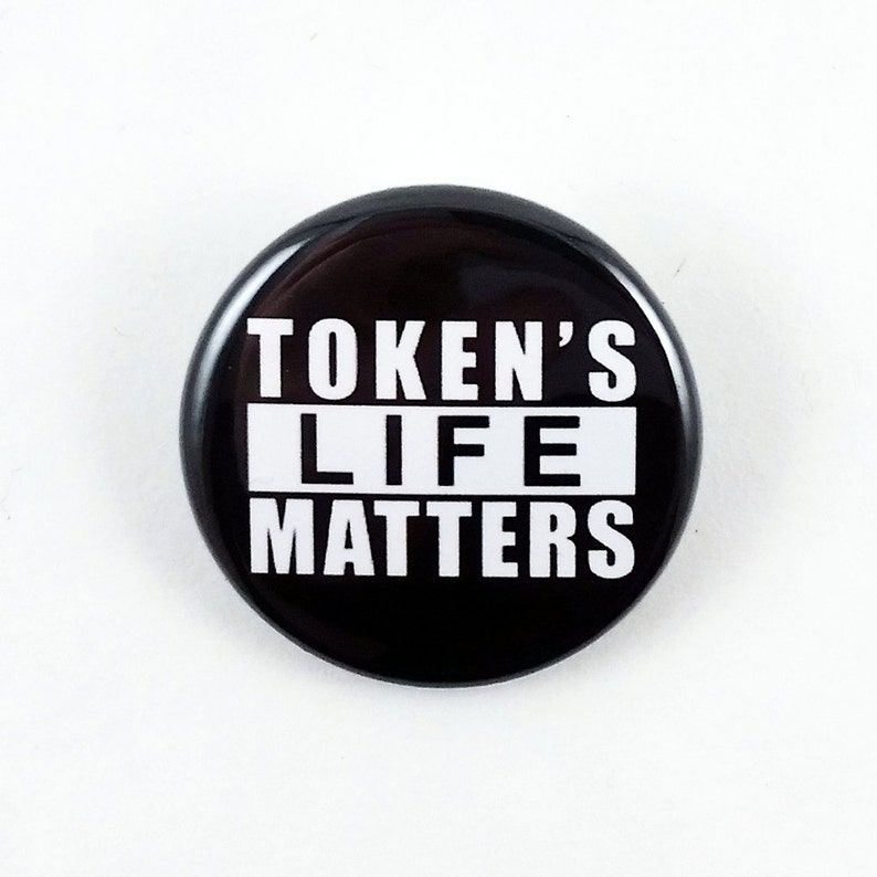 Może przedstawiać: Czarno-biały guzik z tekstem "TOKEN'S LIFE MATTERS" w pogrubionych białych literach.