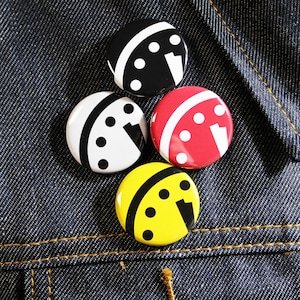 Può includere: Quattro spille rotonde con un design di quadrante dell'orologio in bianco e nero. Le spille sono nere, bianche, gialle e rosse.