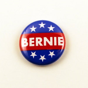 May include: A blue and red button with white stars and the word "BERNIE" in white letters.