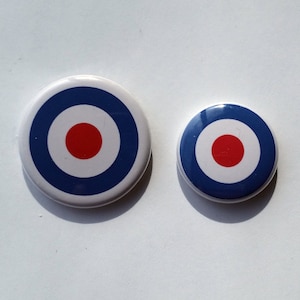 Könnte beinhalten: Zwei runde, zielschießscheibenförmige Knöpfe mit weißem Hintergrund, einem roten Mittelkreis und einem blauen Ring um den Mittelkreis. Der größere Knopf hat einen Durchmesser von etwa 5 cm, der kleinere Knopf einen Durchmesser von etwa 2,5 cm.