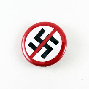 May include: A red and white button with a black swastika symbol crossed out. The button is a symbol of anti-fascism.