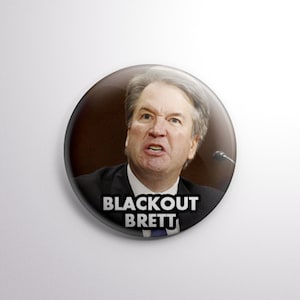 May include: A button featuring a close-up photo of a man with a serious expression. The text "BLACKOUT BRETT" is printed in white letters on a black background.
