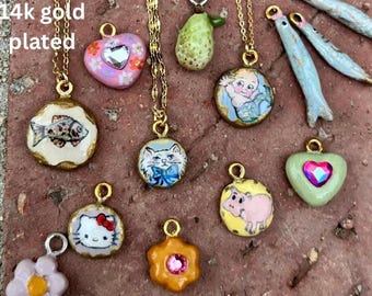 May include: A collection of 14k gold plated pendants on gold chains. The pendants feature various designs, including a fish, a cat, a baby, a pig, a heart, and a flower. The pendants are colorful and detailed.