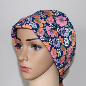 Peut inclure: Une toque chirurgicale bleu marine ornée d'un motif floral rose, orange, violet et blanc. Ce bonnet est conçu pour couvrir la tête et les cheveux, couramment utilisé dans les milieux médicaux. Le tissu est lisse.