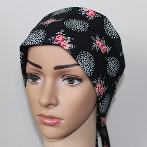 Könnte beinhalten: Ein schwarzes Kopftuch mit einem Blumenmuster aus rosa Rosen und weißen und grauen kreisförmigen Designs. Das Kopftuch ist hinten gebunden und wird auf einem Schaufensterkopf präsentiert.