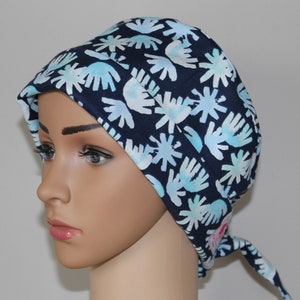 Op de afbeelding: Een marineblauwe chirurgische scrubcap met een herhalend patroon van lichtblauwe en witte abstracte bloemvormen. De cap wordt aan de achterkant vastgebonden en wordt gedragen door een mannequin. De cap is gemaakt van een zachte, lichte stof.