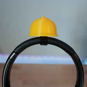 Op de afbeelding: Een gele bouwvakkershelm zit bovenop een zwart hoofdband voor koptelefoon.