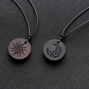 May include: Two necklaces with wooden pendants. One pendant is brown with a sun design, the other is black with a moon design.