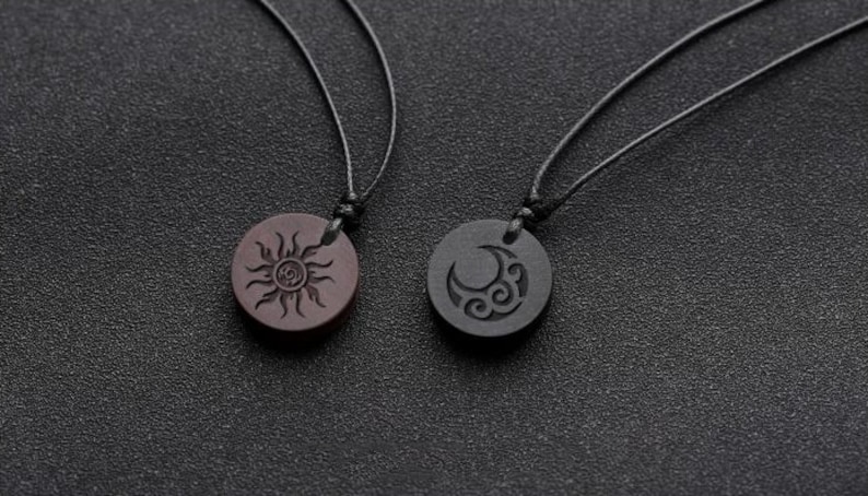 May include: Two necklaces with wooden pendants. One pendant is brown with a sun design, the other is black with a moon design.
