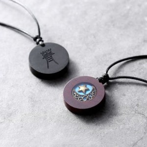 May include: Two necklaces with round wooden pendants. One pendant is black with a Chinese character, the other is brown with a blue and gold star design.