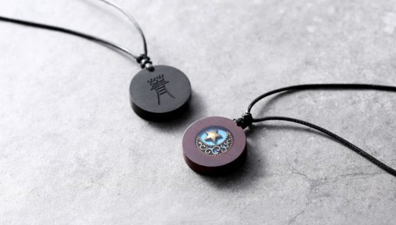 May include: Two necklaces with round wooden pendants. One pendant is black with a Chinese character, the other is brown with a blue and gold star design.