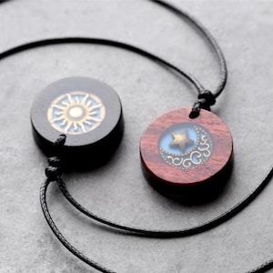 May include: Two wooden necklaces with pendants. One pendant is black with a gold sun design, the other is red with a blue moon and gold star design.