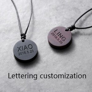 May include: Two black wooden pendants on black cords. The pendants are round and have the names "LING" and "XIAO" engraved on them, along with the date "2018.5.20".