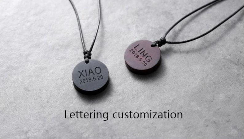 May include: Two black wooden pendants on black cords. The pendants are round and have the names "LING" and "XIAO" engraved on them, along with the date "2018.5.20".