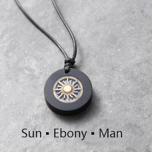 May include: A black necklace with a round ebony pendant featuring a sun design with a gold center.