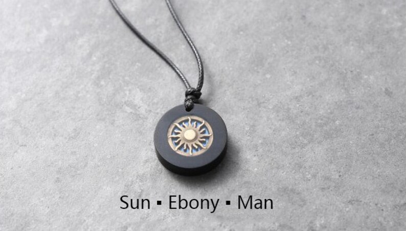 May include: A black necklace with a round ebony pendant featuring a sun design with a gold center.