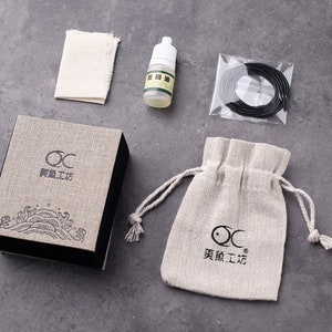 May include: A set of tools for cleaning and maintaining a wooden brush pen. The set includes a small bottle of oil, a cleaning cloth, a small bag, and a roll of black string. The packaging is a brown box with the text "OC 某某工房" printed on it.